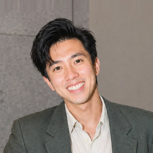 Marcus, in a grey blazer, smiling in front of a concrete wall.